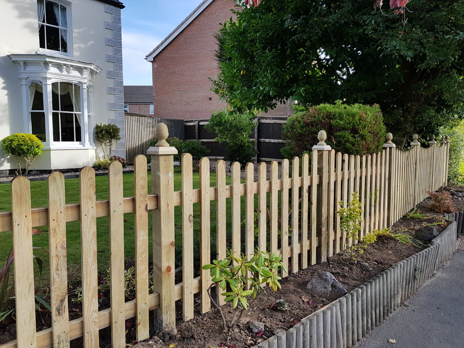 Wooden picket fence in front of a house with greenery
