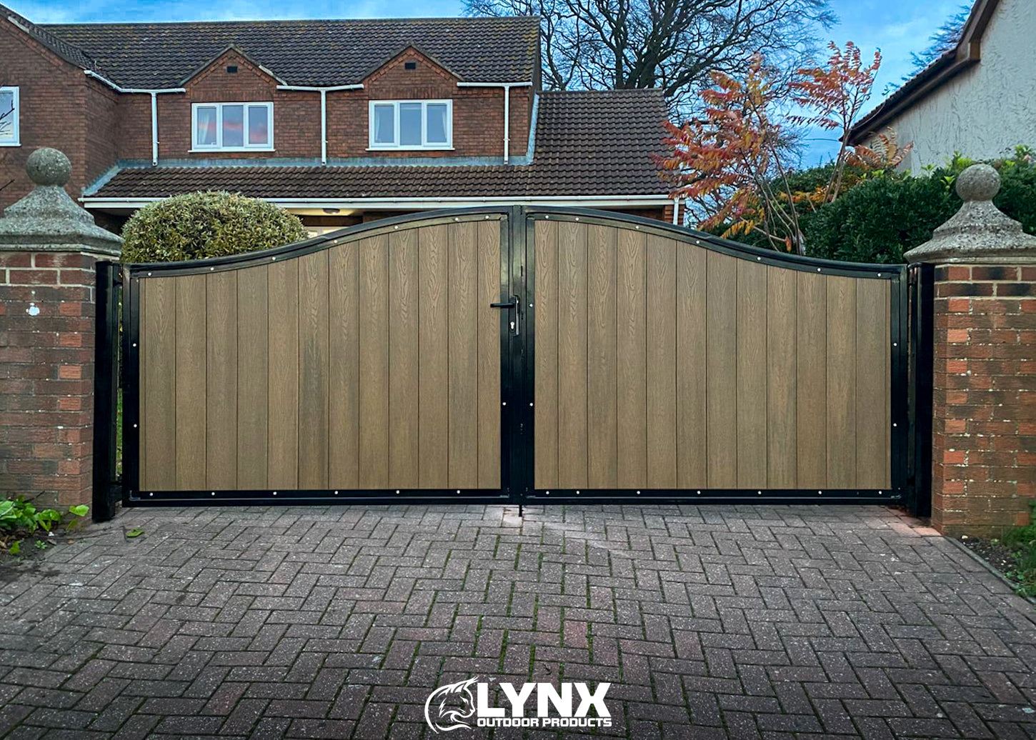 Wooden driveway gate with black frame in front of a house, branded with Lynx Outdoor Products.